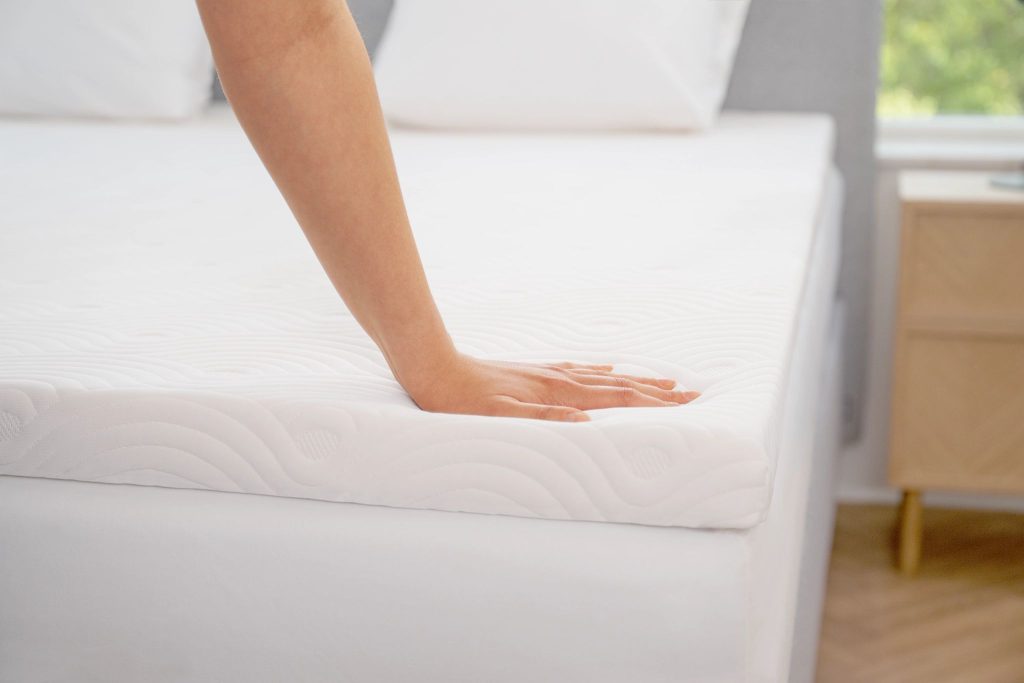 Hand pressing into the TEMPUR ONE Topper on a made bed