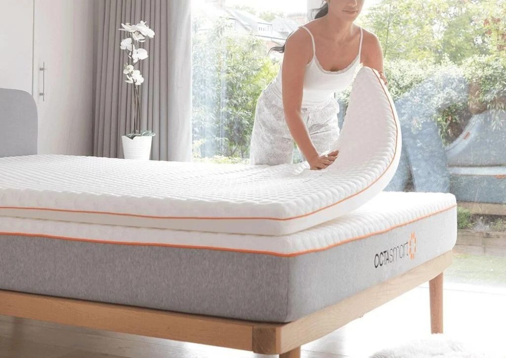 Woman lifting the edge of a Dormeo Octasmart Plus topper on a mattress
