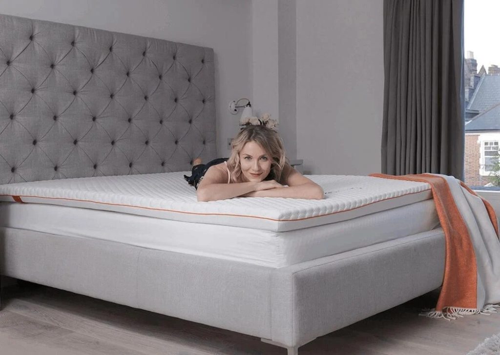 Woman lying on a Dormeo Octasmart Plus topper on a grey upholstered bed