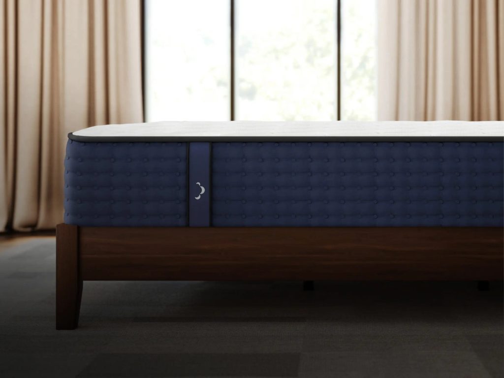 Side view of the DreamCloud Hybrid mattress on a wooden bed frame by a window