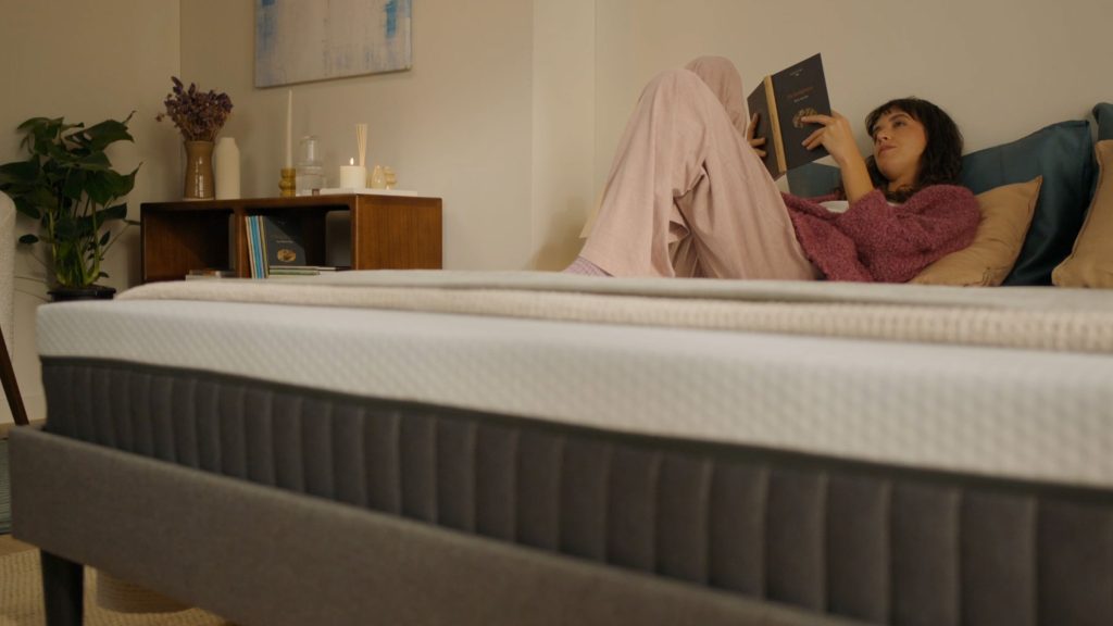 Woman reading on an Emma Original Lite mattress in a cosy bedroom