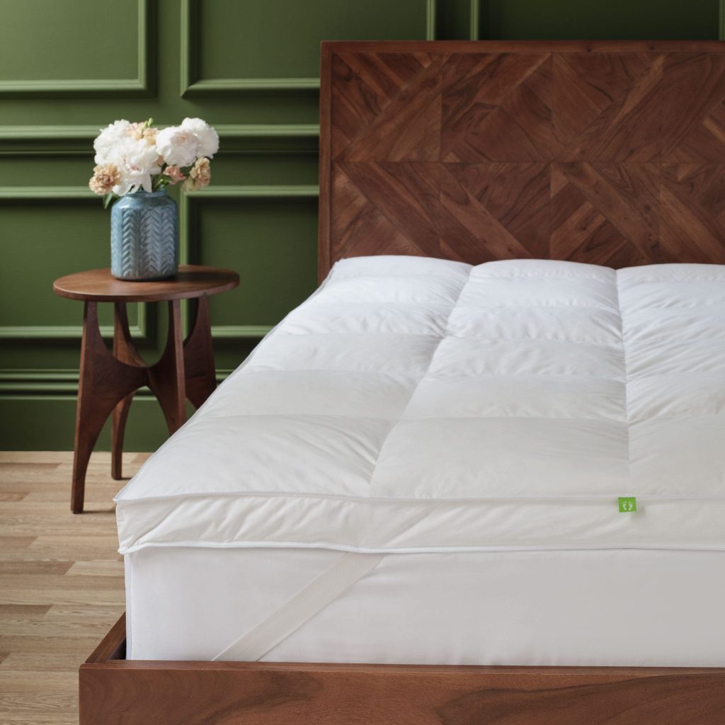 Scooms feather and down topper with its elastic corner strap on a bed in a green room