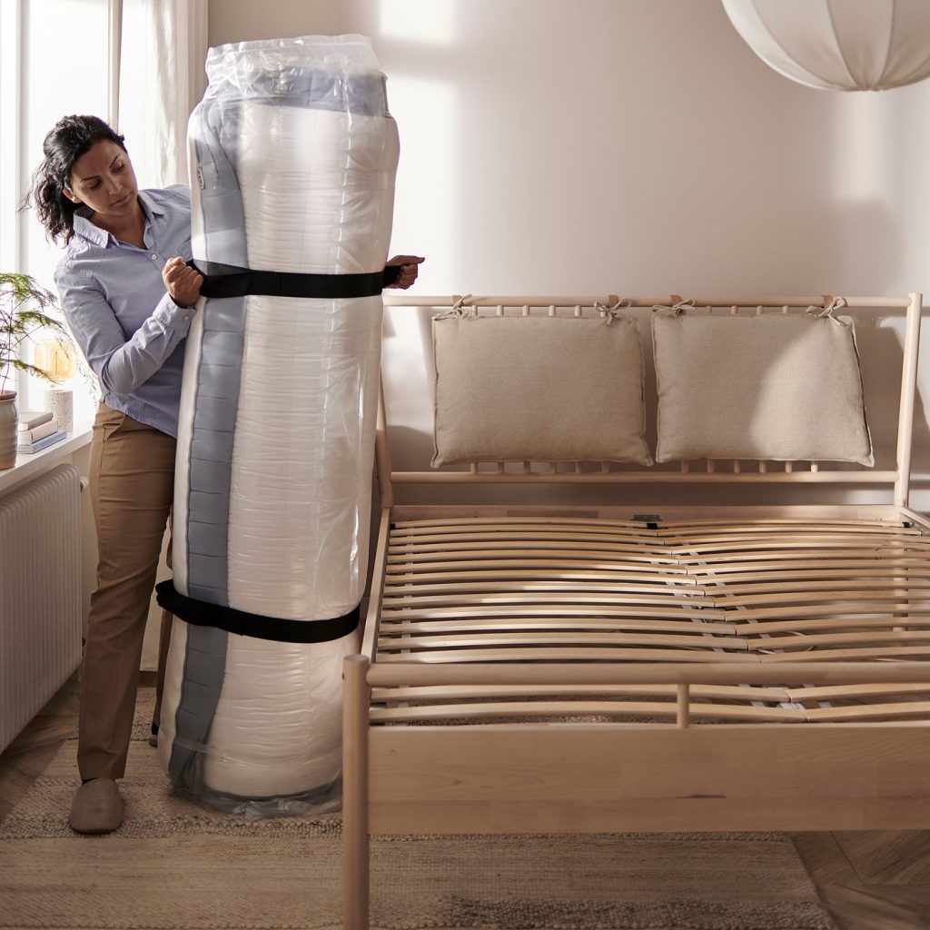 IKEA Valevåg mattress roll-packed and strapped, carried next to a slatted bed base