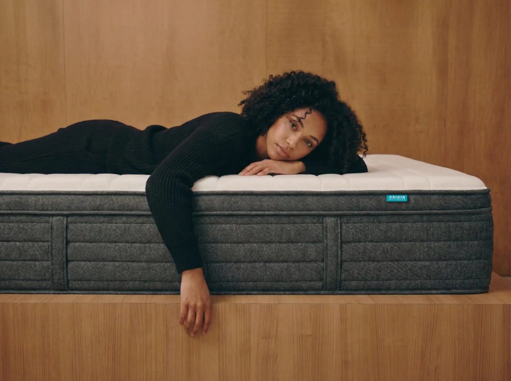 Woman lying across an Origin Hybrid mattress on a wooden platform