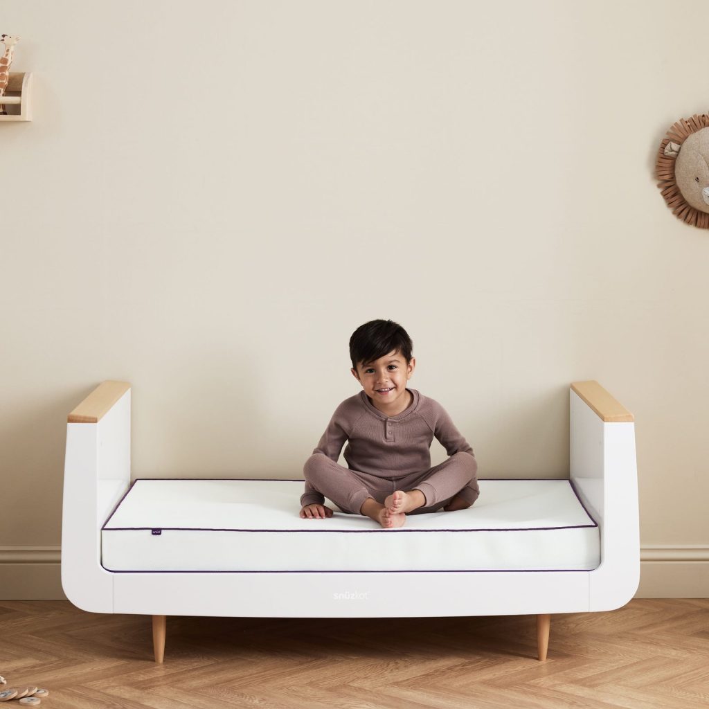Snüz SnuzSurface Duo Cot Bed Mattress in a SnuzKot converted to a toddler bed with a child sitting on it