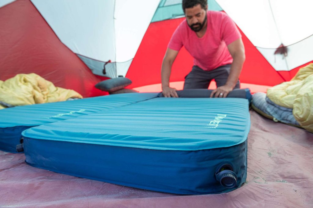 Camper arranging two Therm-a-Rest MondoKing 3D mattresses side by side in a tent
