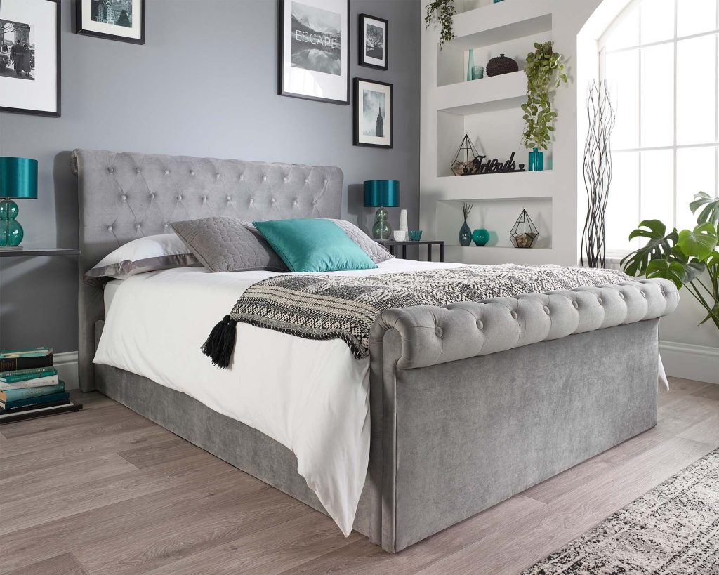 Aspire Scroll Top Chesterfield Ottoman Bed in grey velvet in a grey bedroom