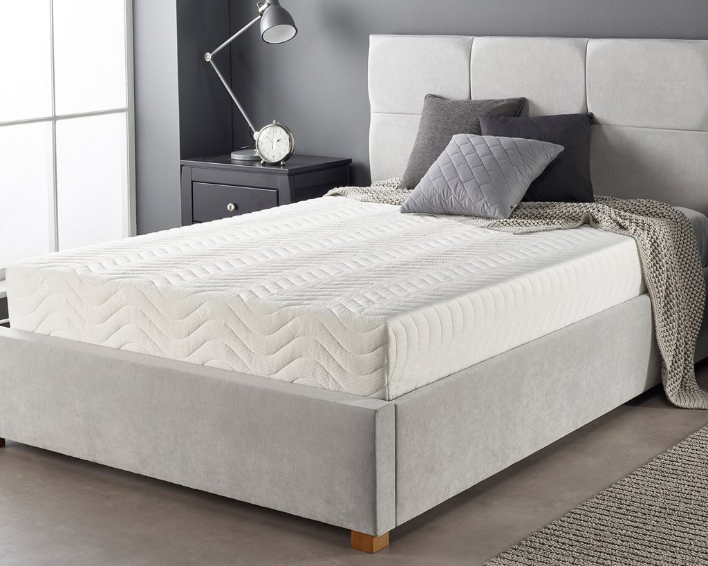 Aspire Total Relief mattress on a grey upholstered bed in a bedroom