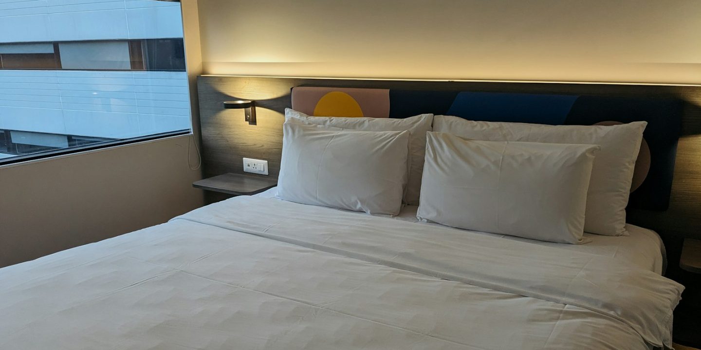 Double bed made up with white bedding and four pillows against a lit wooden headboard