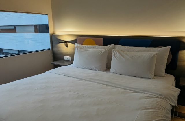 Double bed made up with white bedding and four pillows against a lit wooden headboard