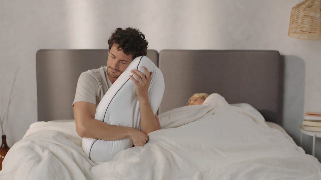 Man sitting up in bed hugging an Emma Adapt Pillow
