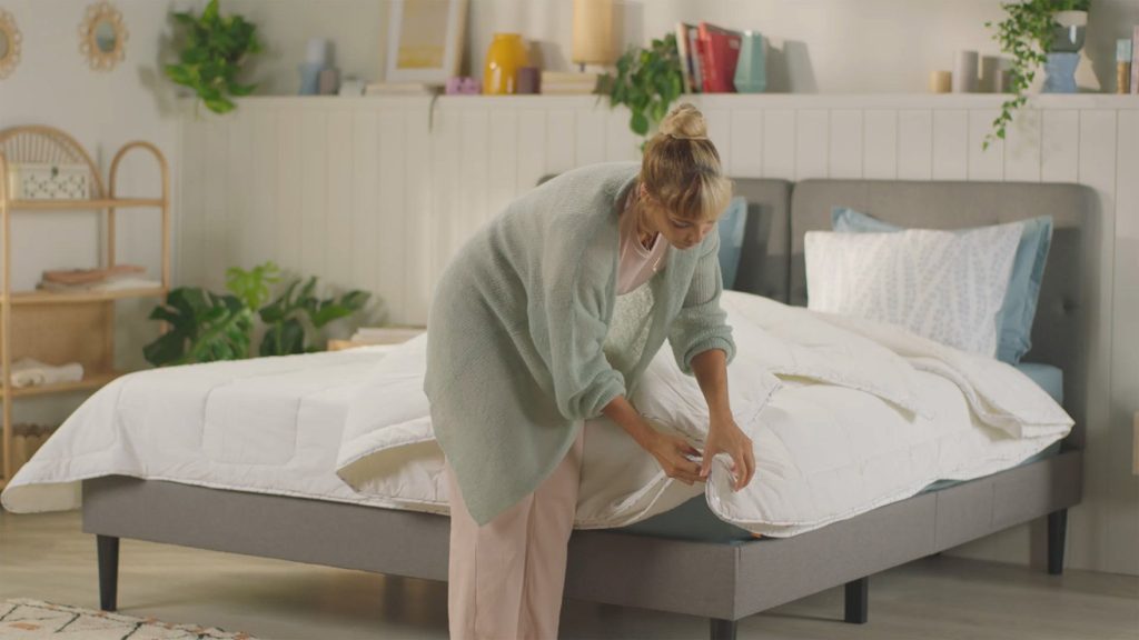 Woman spreading the Emma All Seasons duvet over a bed