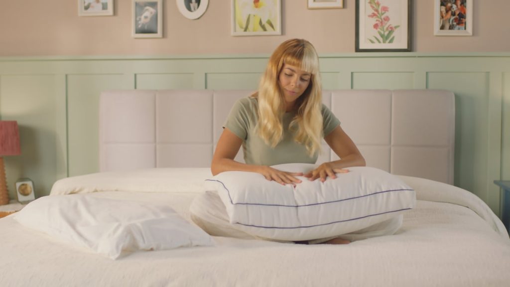 Woman sitting on a bed adjusting the inner layers of an Emma Comfort Cooling Pillow