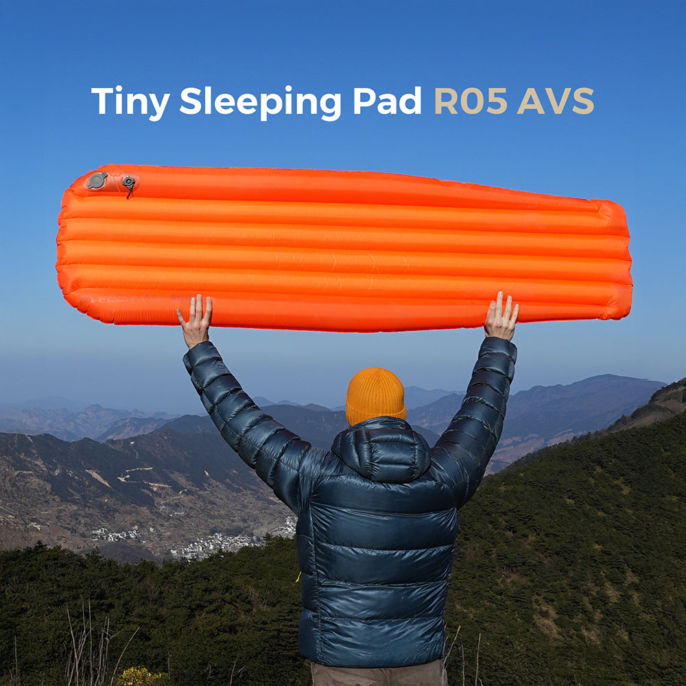 Camper holding up an inflated Flextail Tiny Sleeping Pad R05 AVS camping mattress in the mountains