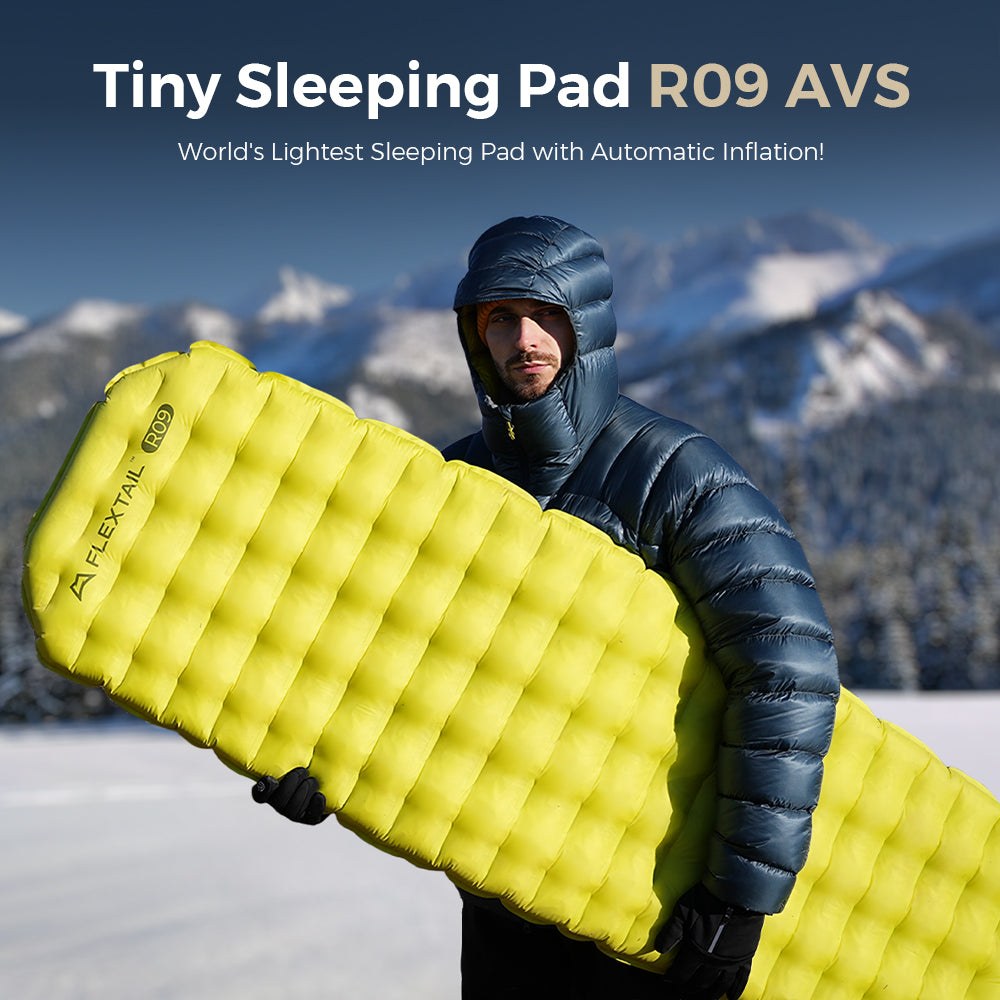 Camper in snowy mountains holding an inflated Flextail Tiny Sleeping Pad R09 AVS