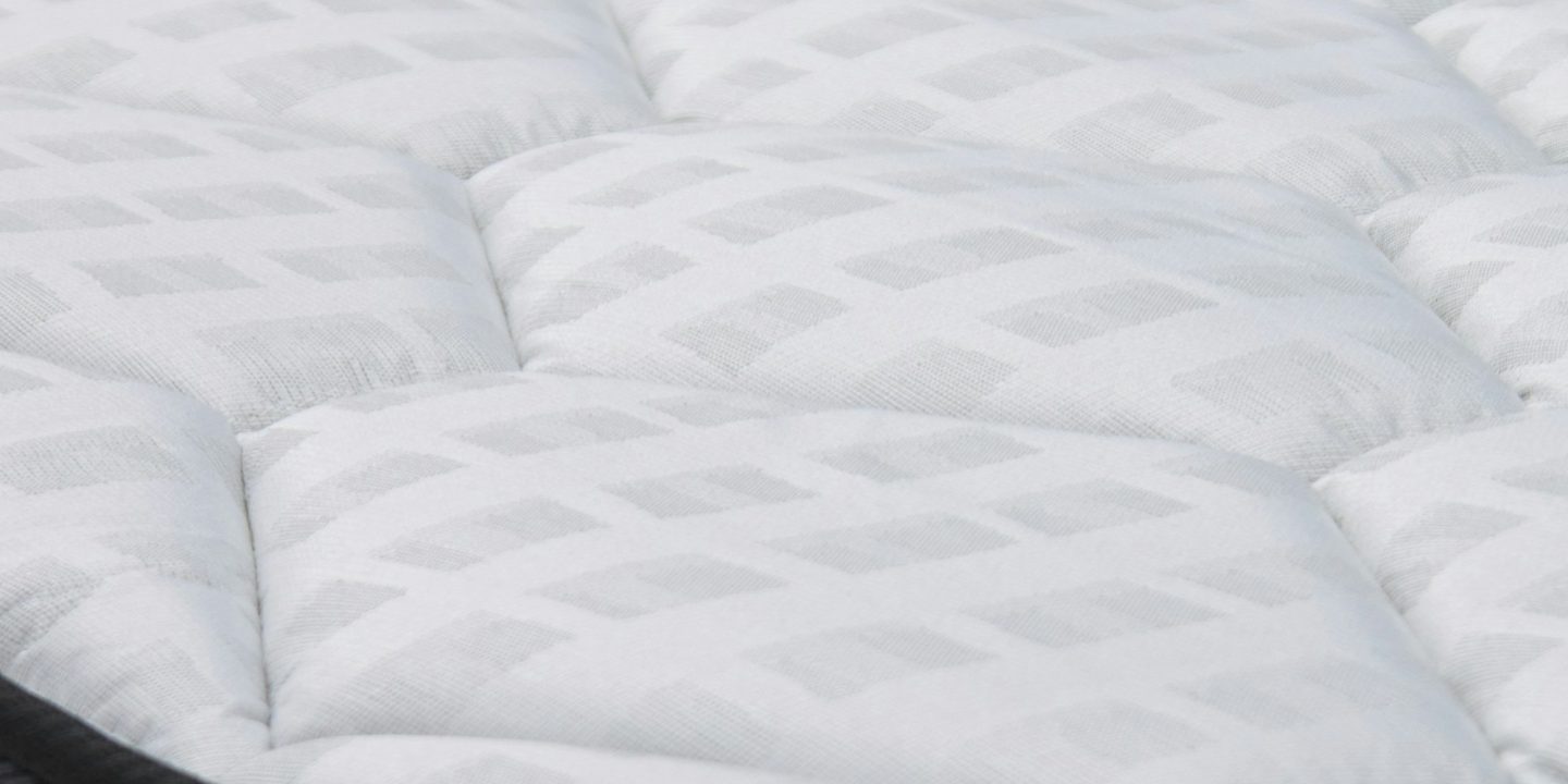 Close-up of the quilted white top panel of a mattress with a dark grey border