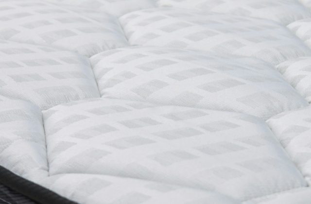 Close-up of the quilted white top panel of a mattress with a dark grey border
