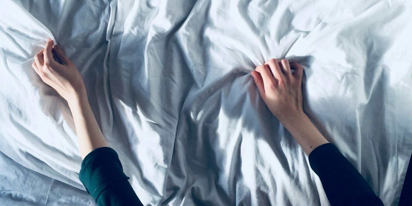 Two hands pulling back a crumpled white sheet to strip a bed before cleaning the mattress