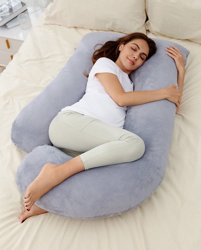 Pregnant woman sleeping on her side inside the Momcozy Huggable U-shaped pillow on a bed