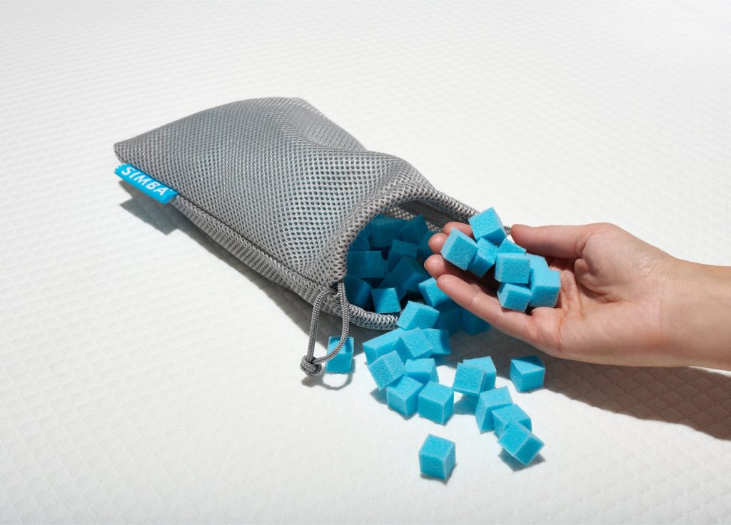 Hand taking blue foam Nanocubes out of the grey mesh bag supplied with the Simba Hybrid Pillow