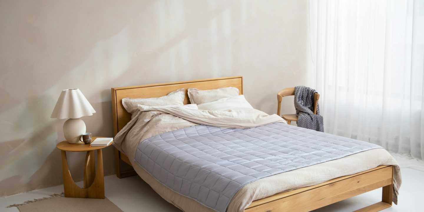 Double bed on an oak frame with a bedside table, lamp and chair in a bright bedroom