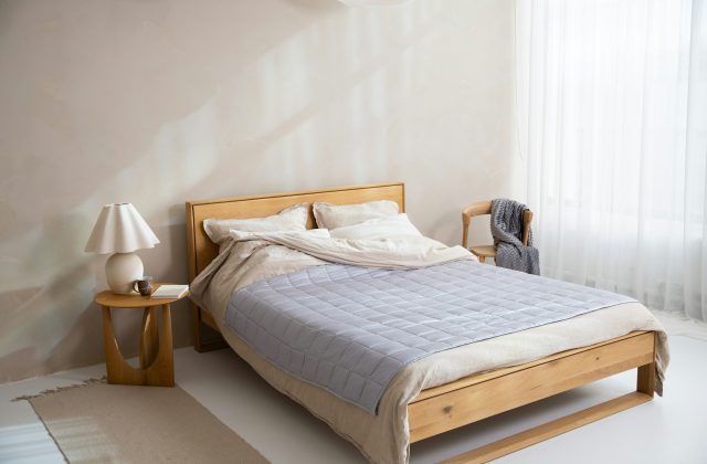 Double bed on an oak frame with a bedside table, lamp and chair in a bright bedroom